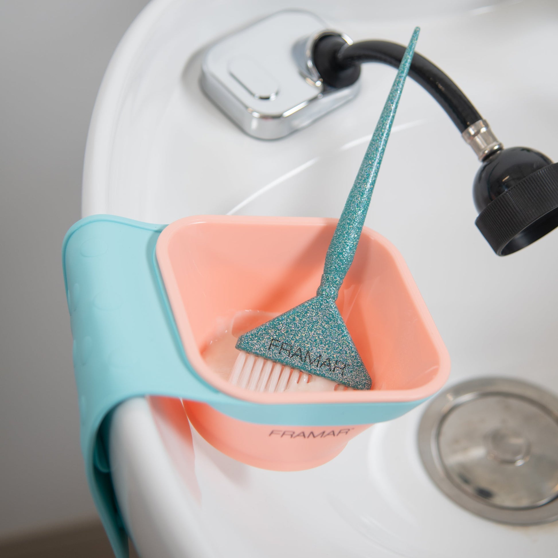 Pet grooming tool with a pink basin and blue handle attached to a sink.