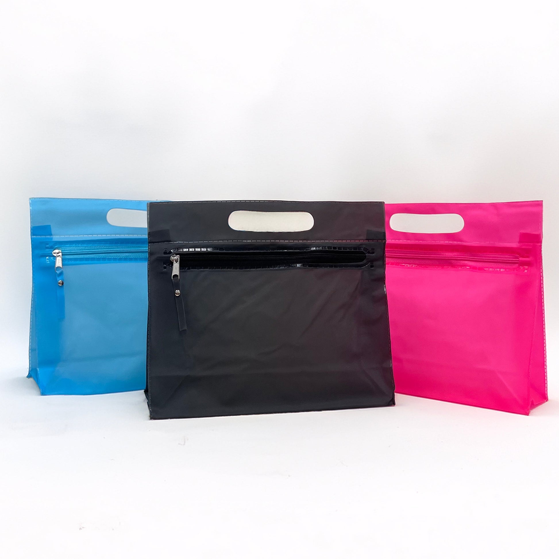 Three zip-top pouches with die-cut handles in blue, black, and pink, arranged side-by-side on a white studio background.